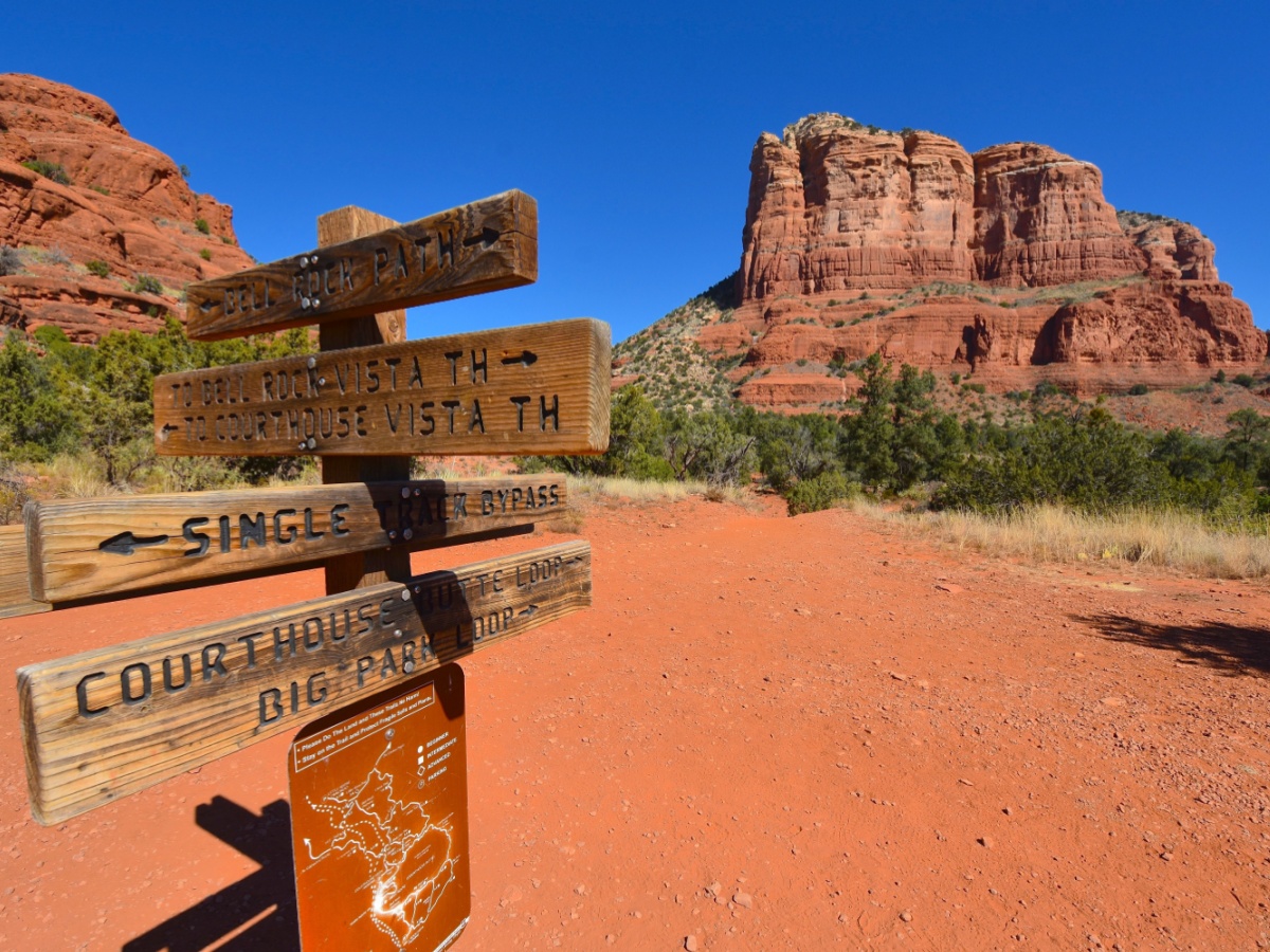 A post with wooden signs that have the arrows pointing to the direction of the hiking path.