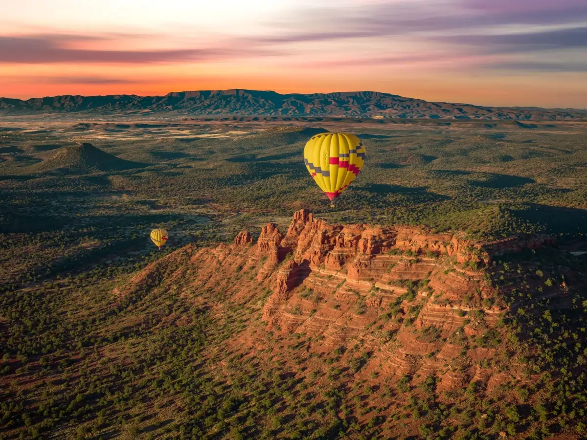 Colorful hot air balloon floating above Sedona’s expansive red rock canyons and mesas at sunrise, showcasing sweeping desert vistas and layered cliffs.
