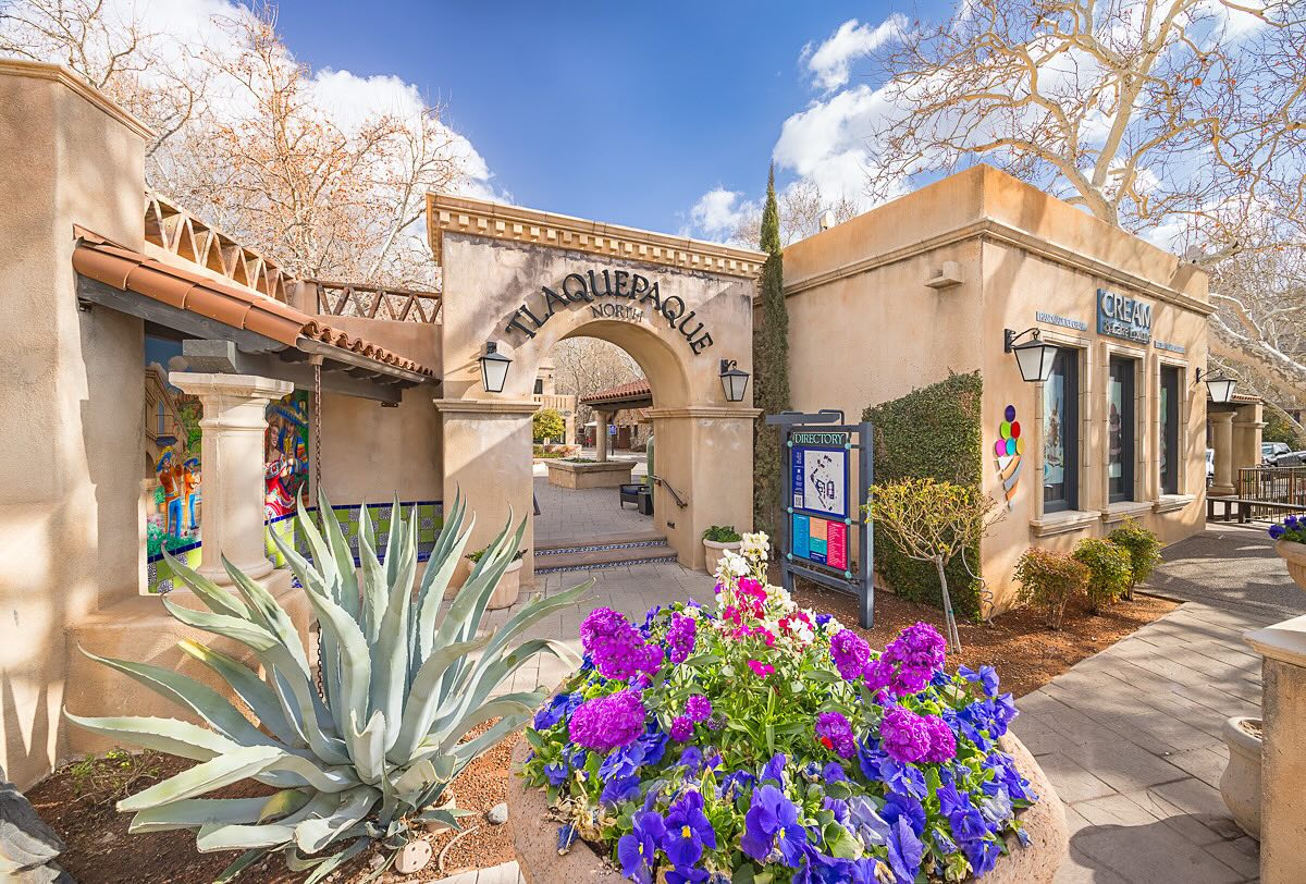 Tlaquepaque shopping complex with purple flowers and some green plants out front.