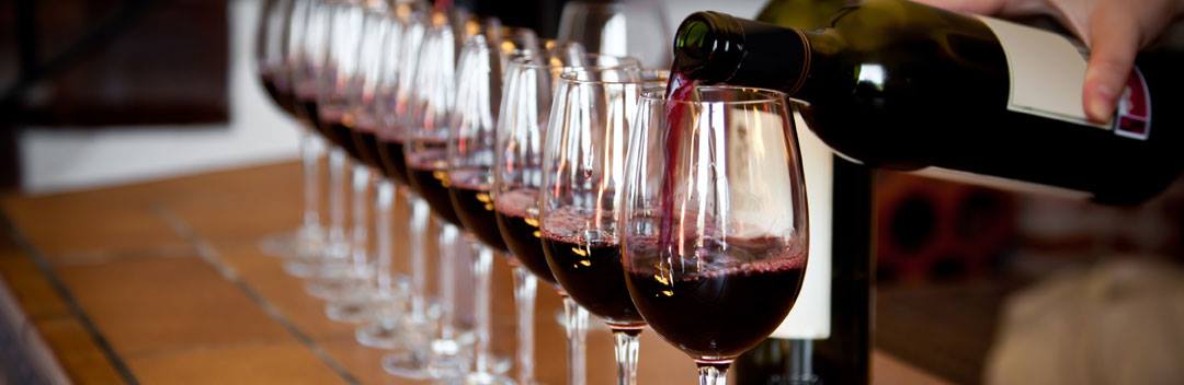 A row of wine glasses with wine being poured in them.